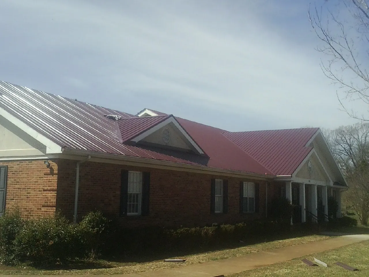 Red metal roof with gabled entries on a long brick building, from a Hail Damage Roof Repair job in Scotts Mills