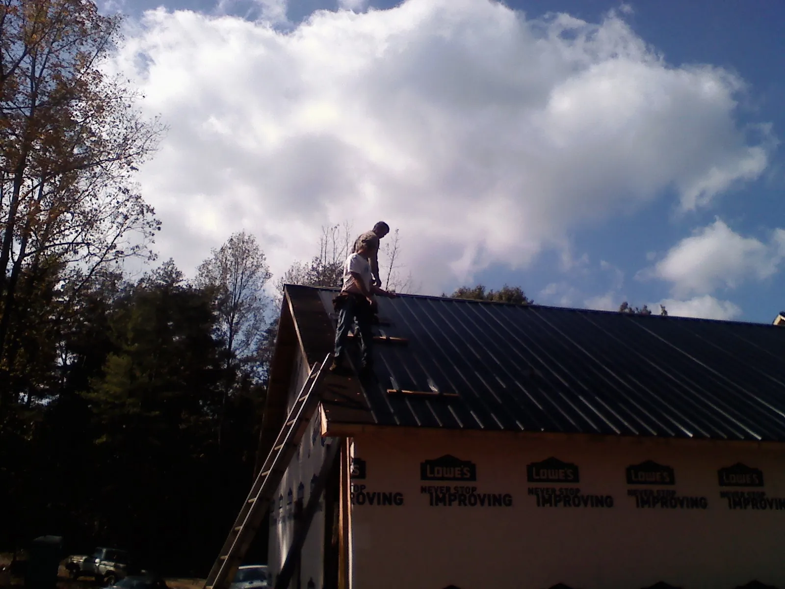 Roofer fastening dark metal panels high against a cloudy sky, from a Roof Inspection job in Scotts Mills