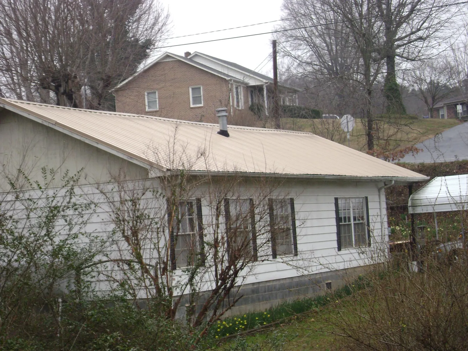 Tan metal roof on a white sided house set into a hillside — Commercial Roofing by Roofing Brothers in Scotts Mills